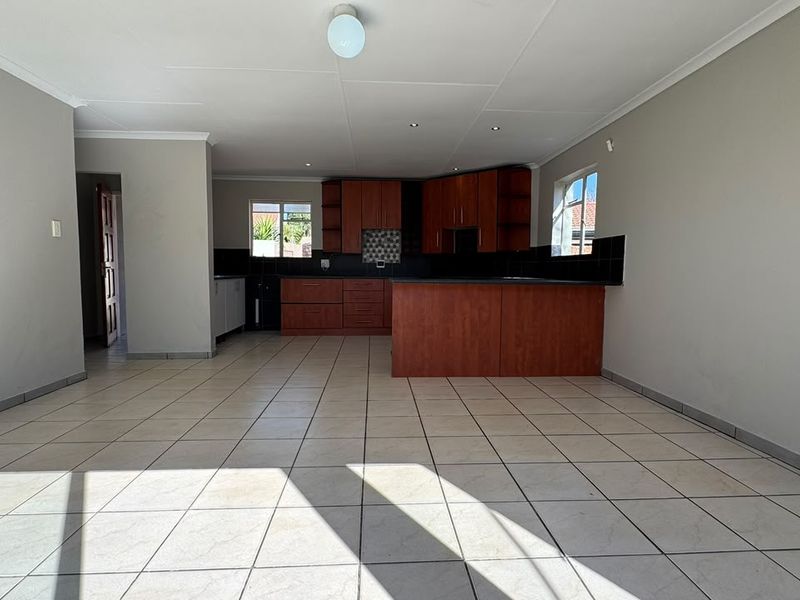 Spacious open-plan living area featuring a functional kitchen with built-in cabinetry, a central island, and neutral tiled flooring throughout.