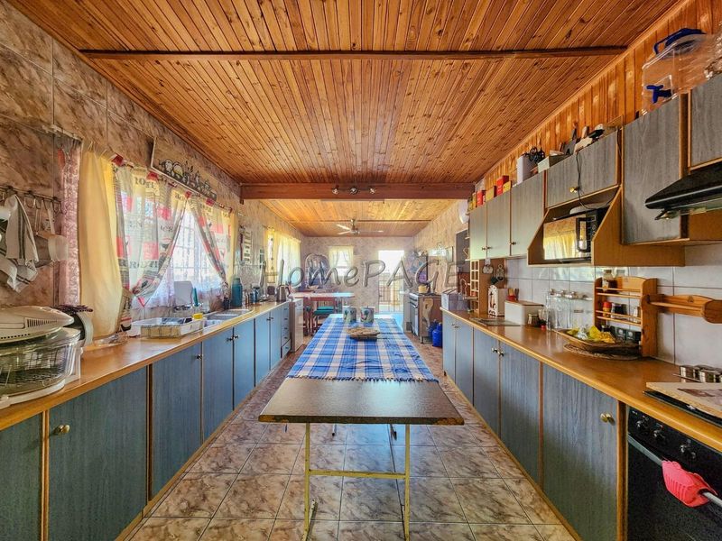 Spacious galley-style kitchen featuring extensive built-in cabinetry, laminate countertops, tiled flooring, and a distinctive timber-clad ceiling.