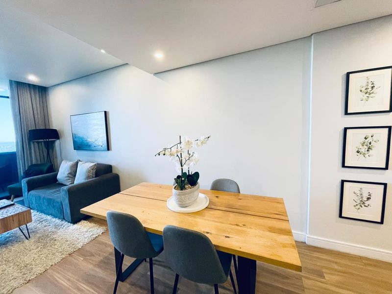 A bright open-plan living and dining area featuring modern laminate flooring, recessed lighting, and direct access to a balcony through sliding glass doors.