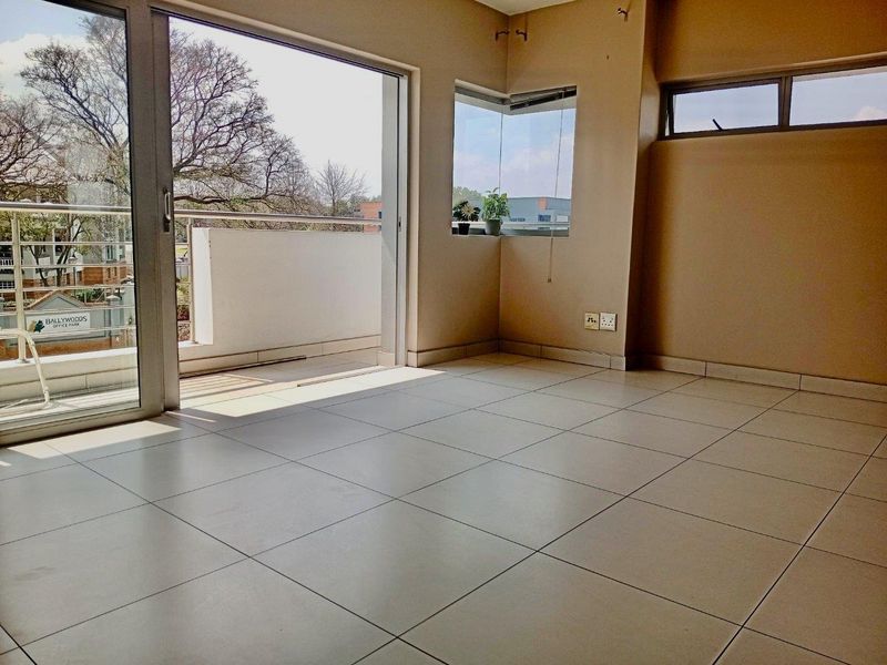 An empty, sunlit living area featuring neutral tiled flooring, a corner window, and large sliding glass doors providing direct access to a private balcony.