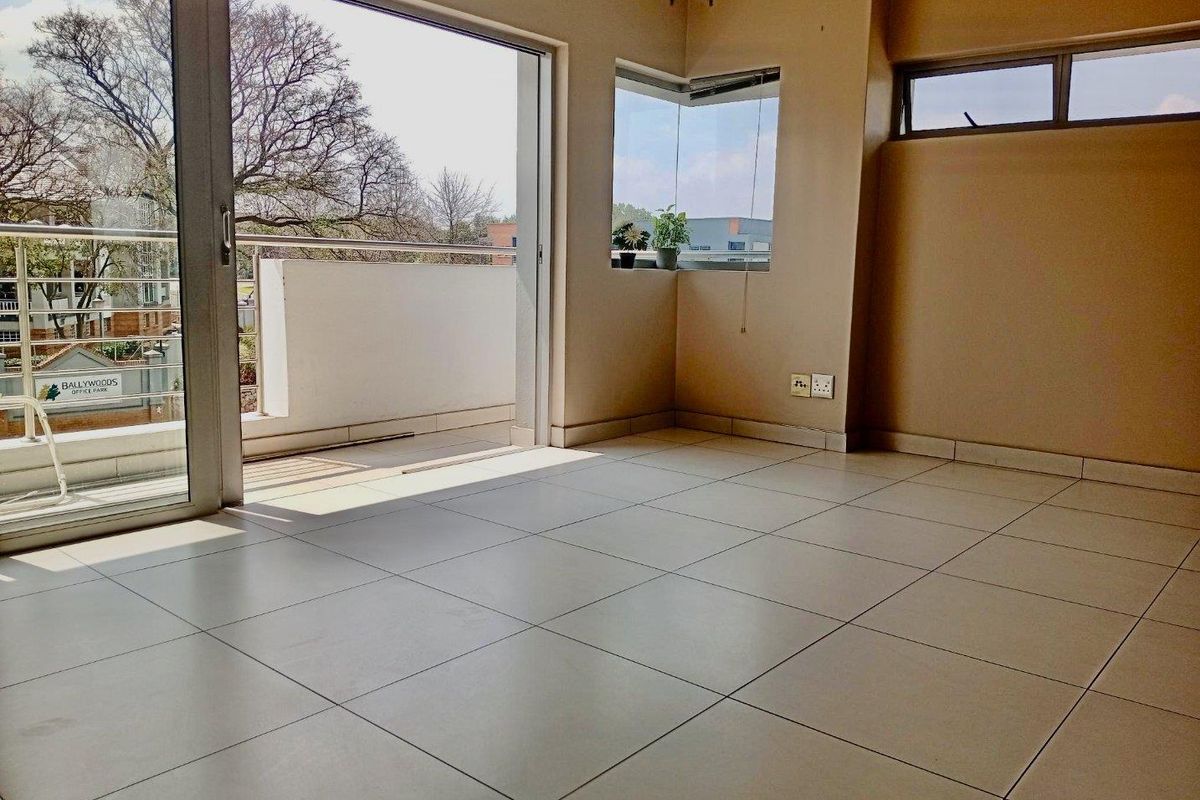 An empty, sunlit living area featuring neutral tiled flooring, a corner window, and large sliding glass doors providing direct access to a private balcony.