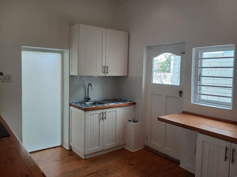 A functional scullery or utility area featuring white cabinetry, wooden countertops, a stainless steel sink, and direct access to the exterior.