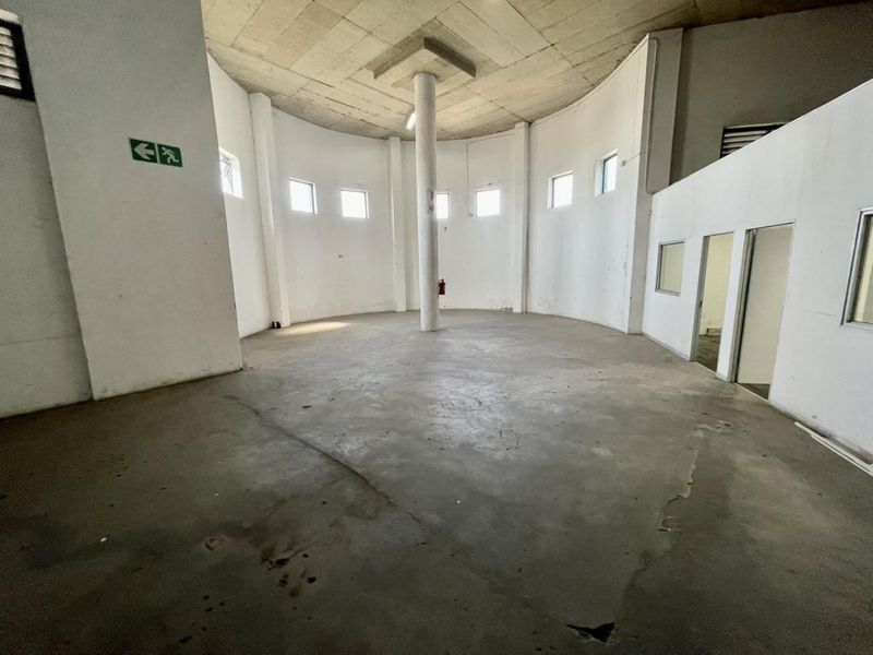 A spacious, empty industrial utility area featuring a central support column, exposed concrete ceiling, and polished concrete flooring with visible wear.