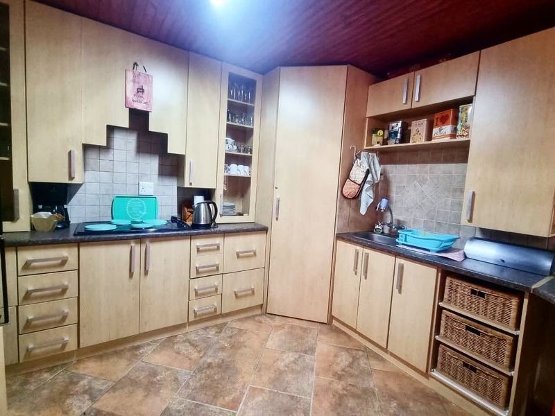 A functional kitchen featuring light wood-finish cabinetry, tiled backsplash, laminate countertops, and integrated sink, offering a practical layout for daily meal preparation.