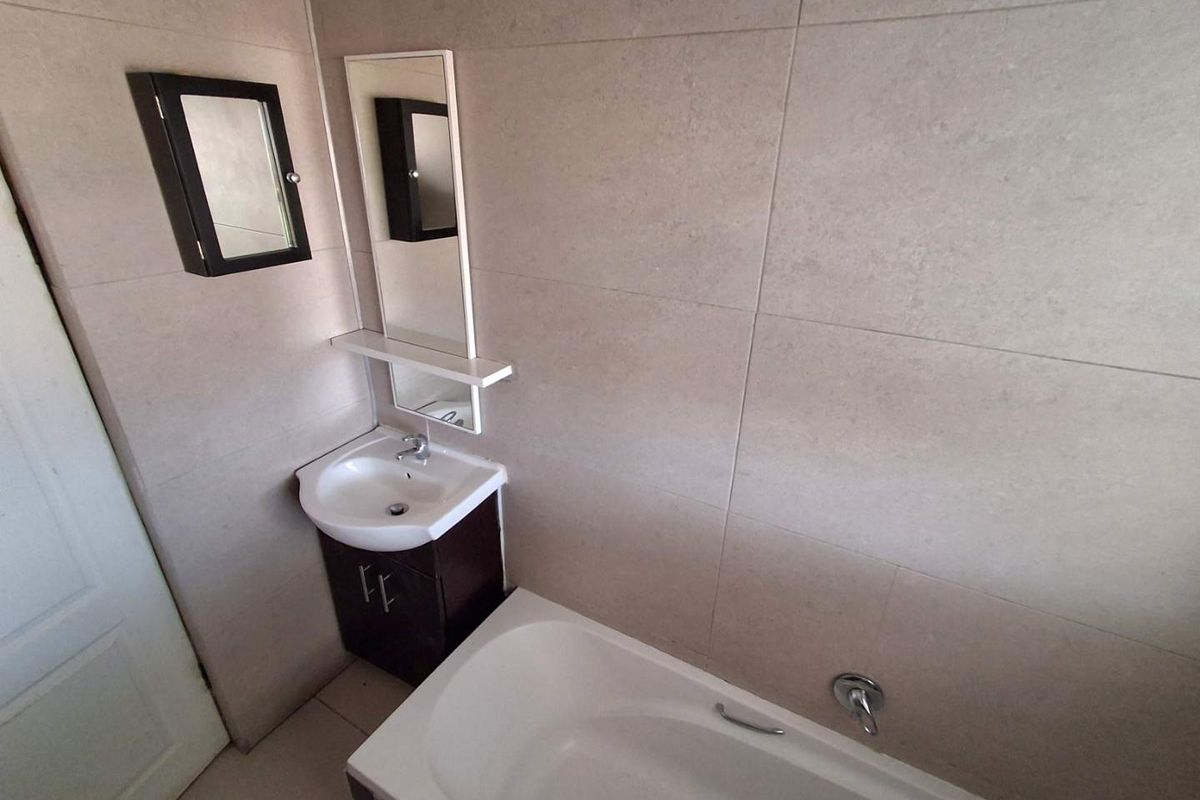 A modern bathroom featuring large-format wall tiles, a built-in bathtub, and a vanity unit with a basin and mirror.