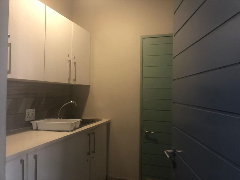A compact scullery or kitchenette area featuring white built-in cabinetry, a sink, and a tiled backsplash.