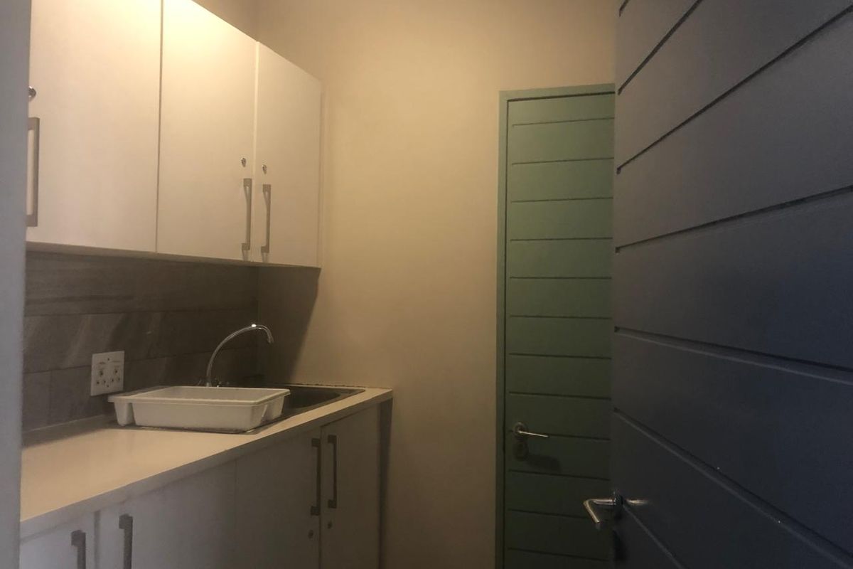 A compact scullery or kitchenette area featuring white built-in cabinetry, a sink, and a tiled backsplash.