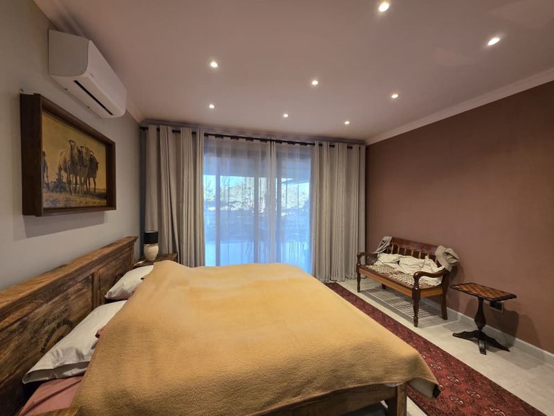 A well-maintained bedroom featuring recessed ceiling lighting, a wall-mounted air conditioning unit, and large sliding glass doors leading to an outdoor area.