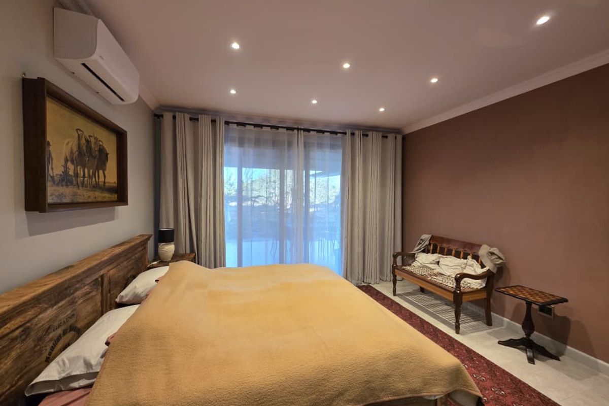 A well-maintained bedroom featuring recessed ceiling lighting, a wall-mounted air conditioning unit, and large sliding glass doors leading to an outdoor area.