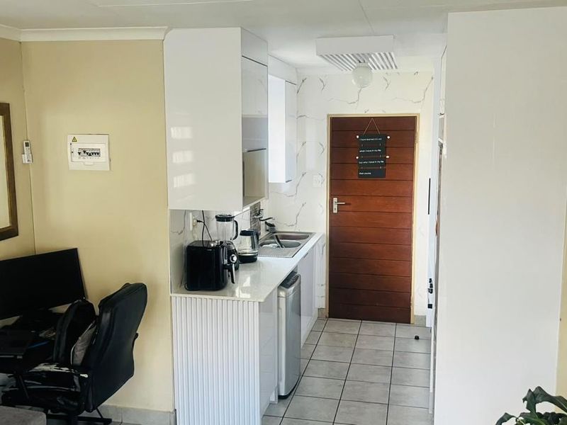 Compact kitchen area featuring white cabinetry, tiled flooring, and an integrated sink, adjacent to a living space with wall-mounted air conditioning.