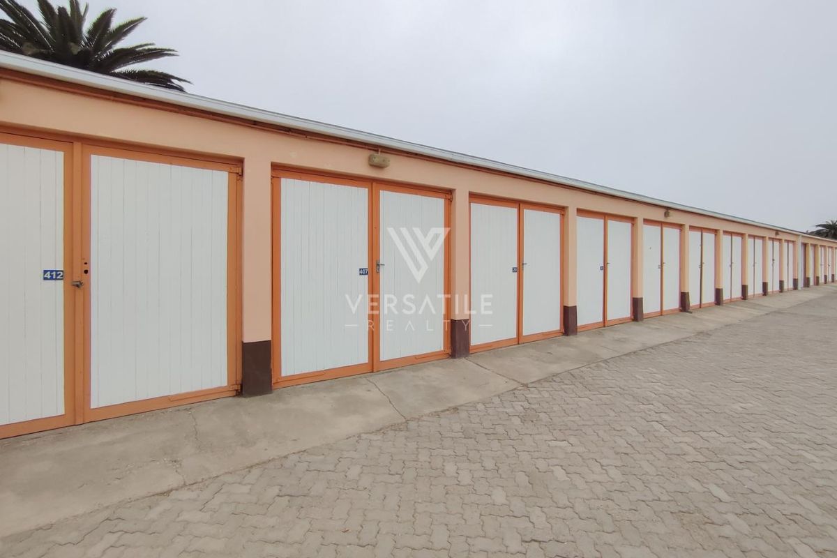 A row of multiple individual garage units with white doors and orange frames, situated along a paved driveway in a retirement village setting.