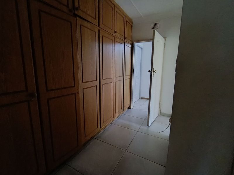 A bedroom featuring extensive built-in wooden cabinetry and neutral tiled flooring, leading into an adjacent hallway.