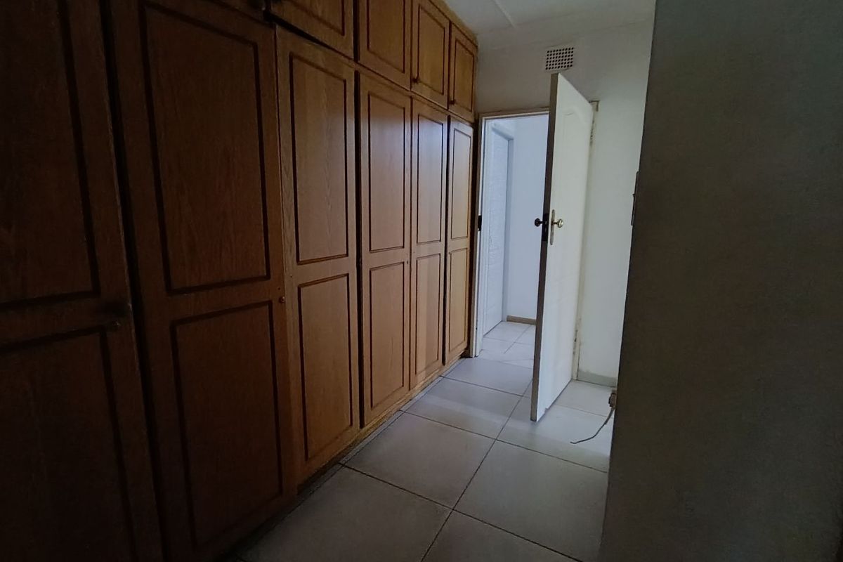 A bedroom featuring extensive built-in wooden cabinetry and neutral tiled flooring, leading into an adjacent hallway.