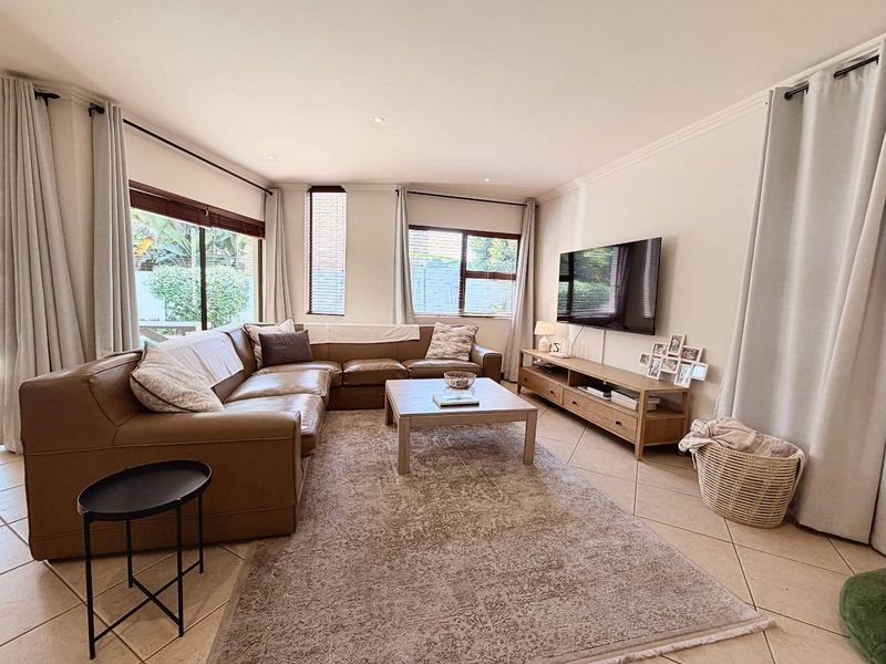 A bright and spacious living room featuring neutral tiled flooring, recessed lighting, and large windows that provide ample natural light.