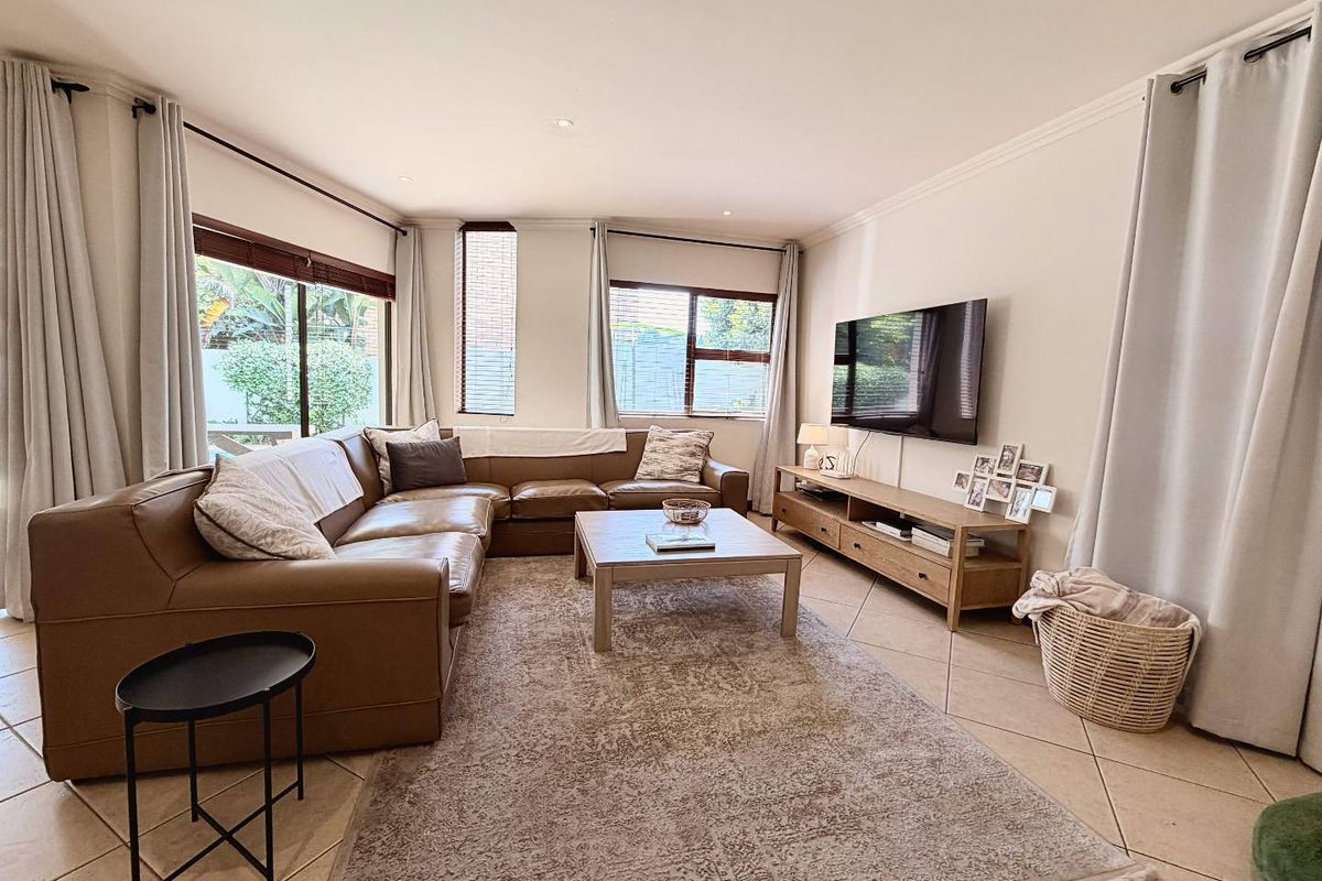 A bright and spacious living room featuring neutral tiled flooring, recessed lighting, and large windows that provide ample natural light.