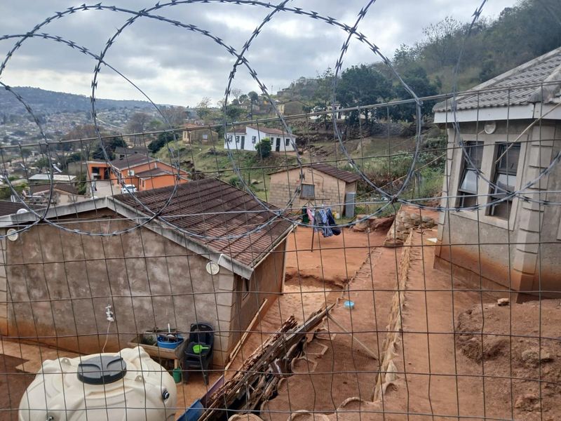 Rear exterior view of the property featuring a tiled roof, water storage tank, and security fencing overlooking the surrounding neighbourhood.