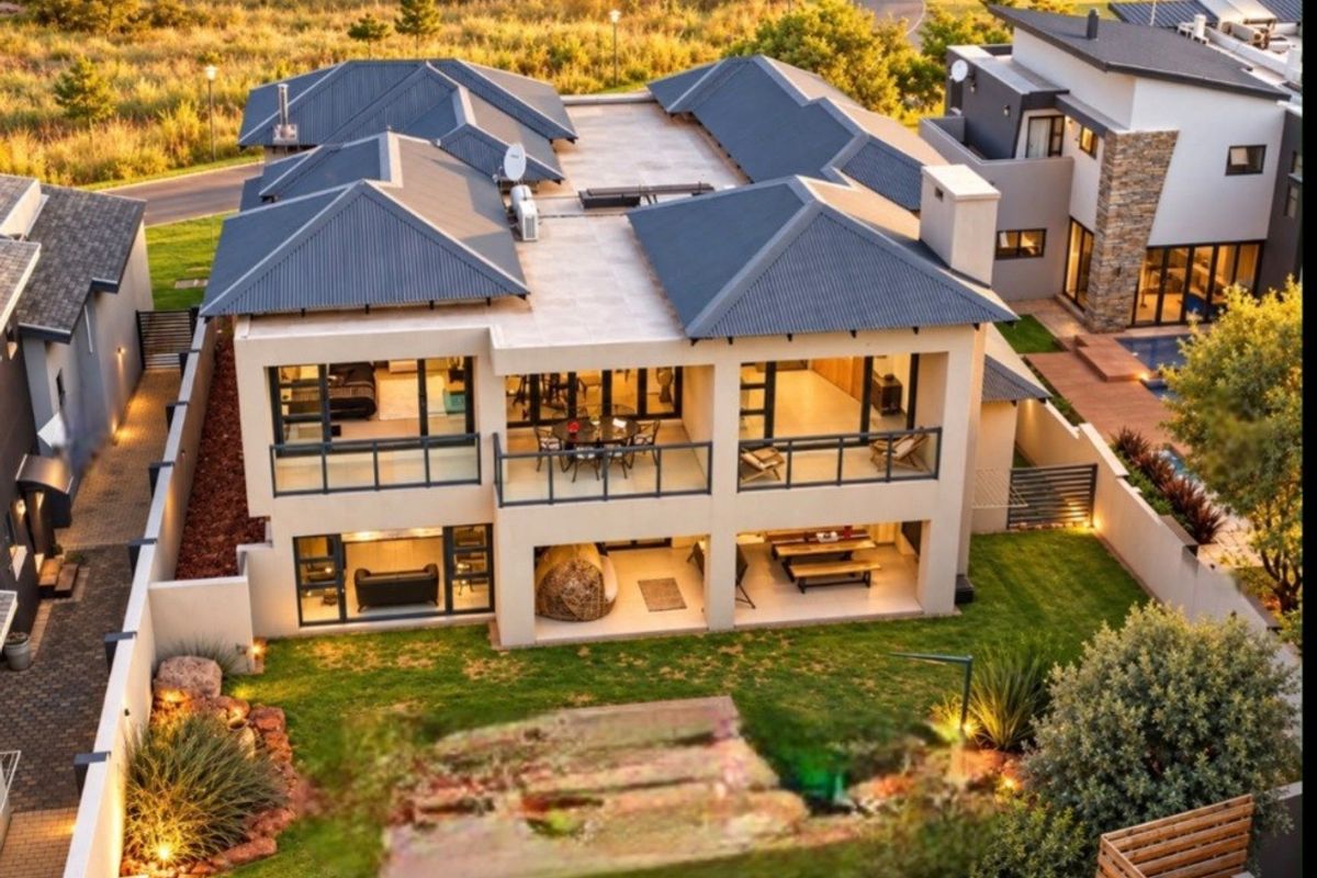 Aerial view of a modern double-story residence featuring a corrugated metal roof, spacious balconies, a covered patio, and a well-maintained garden.