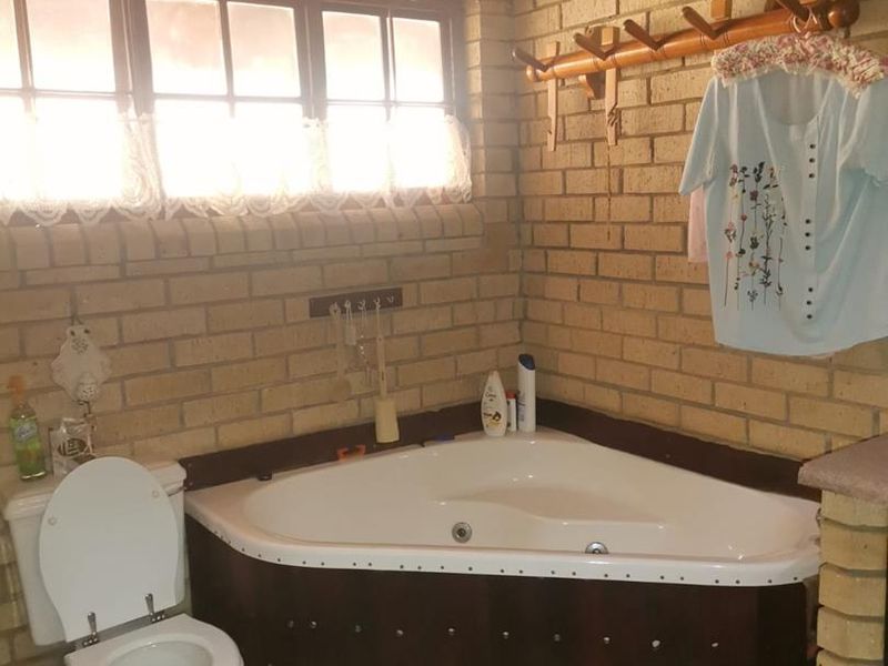 Bathroom featuring exposed brick walls, a corner spa bath, and a timber-framed window, offering a rustic aesthetic.