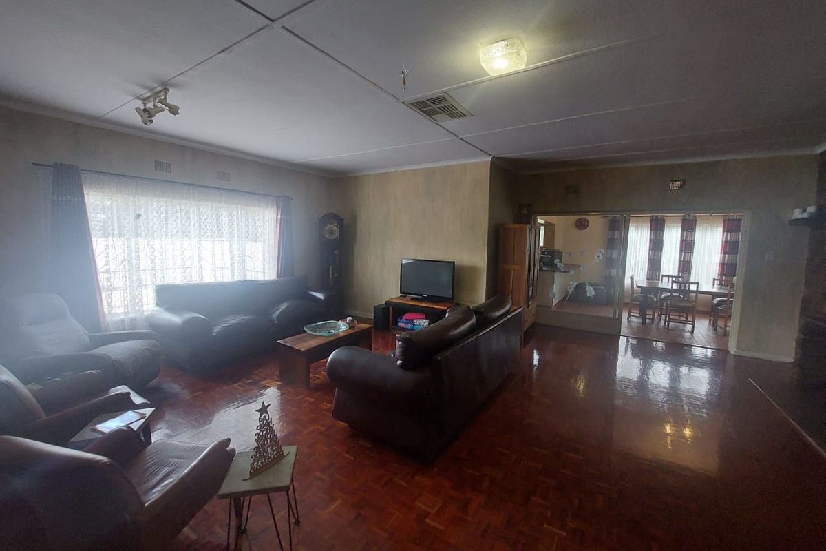 Spacious living room featuring traditional parquet flooring and a large window, with an adjacent dining area visible through a glass partition.