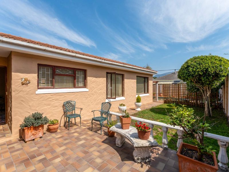 A paved outdoor patio area featuring a balustrade, overlooking a small garden space with established trees and boundary fencing.