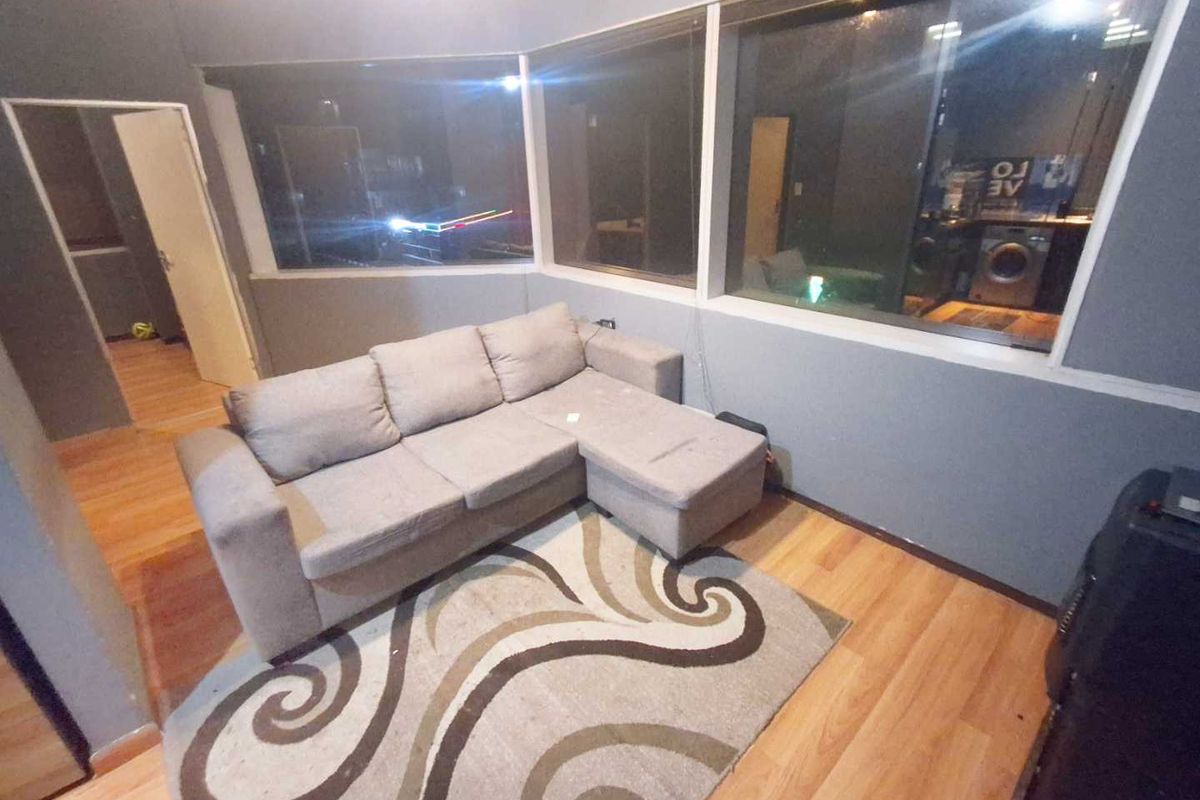 A living room area featuring laminate flooring and large windows, providing natural light and a view into the adjacent space.