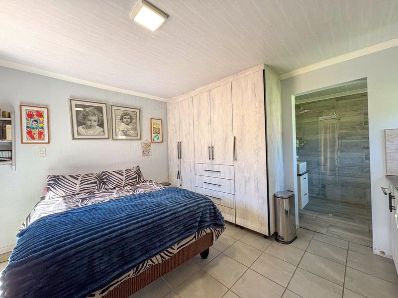 A bedroom featuring built-in wardrobes, tiled flooring, and an adjoining en-suite bathroom with a glass-enclosed shower.