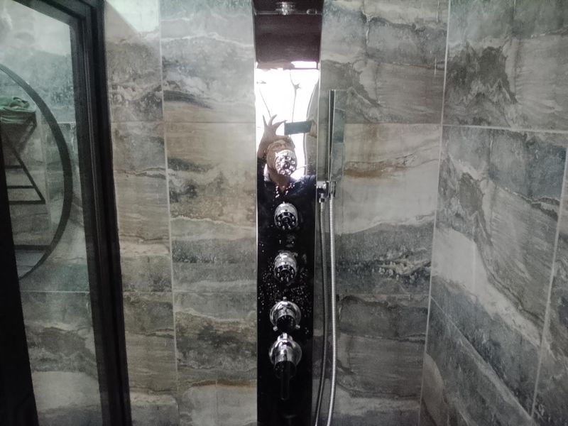 A modern bathroom shower enclosure featuring a sleek, multi-jet shower panel with a handheld attachment and contemporary stone-look wall tiling.