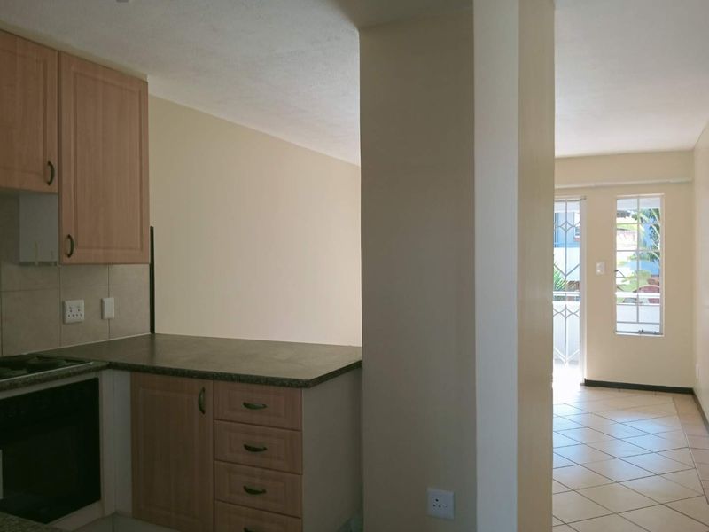 Open plan kitchen area featuring laminate cabinetry and tiled flooring, leading into a bright living space with access to an outdoor area.
