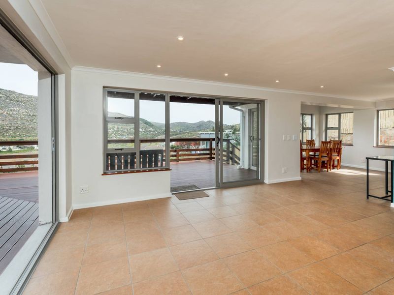 Spacious open-plan living area featuring neutral tiled flooring, recessed lighting, and large sliding doors opening onto an expansive outdoor deck with scenic views.
