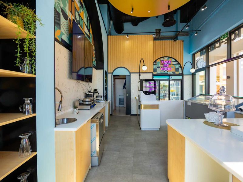 A modern, vibrant commercial kitchen space featuring built-in cabinetry, stainless steel fixtures, display refrigeration, and contemporary decorative wall finishes.