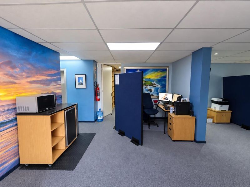 An open-plan office space featuring a suspended ceiling, recessed lighting, and a dedicated kitchenette area with a mural wall.
