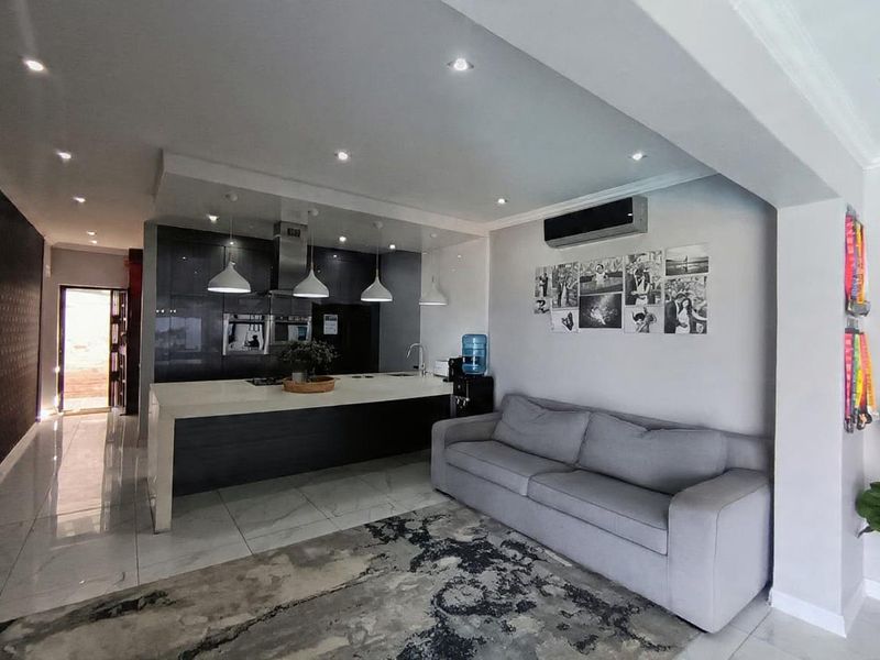 Modern open-plan living area featuring a sleek kitchen with a large island, built-in appliances, and contemporary recessed lighting throughout the space.