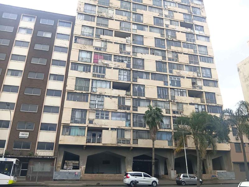Exterior view of a multi-story apartment building featuring a concrete facade with visible signs of weathering and paint deterioration.