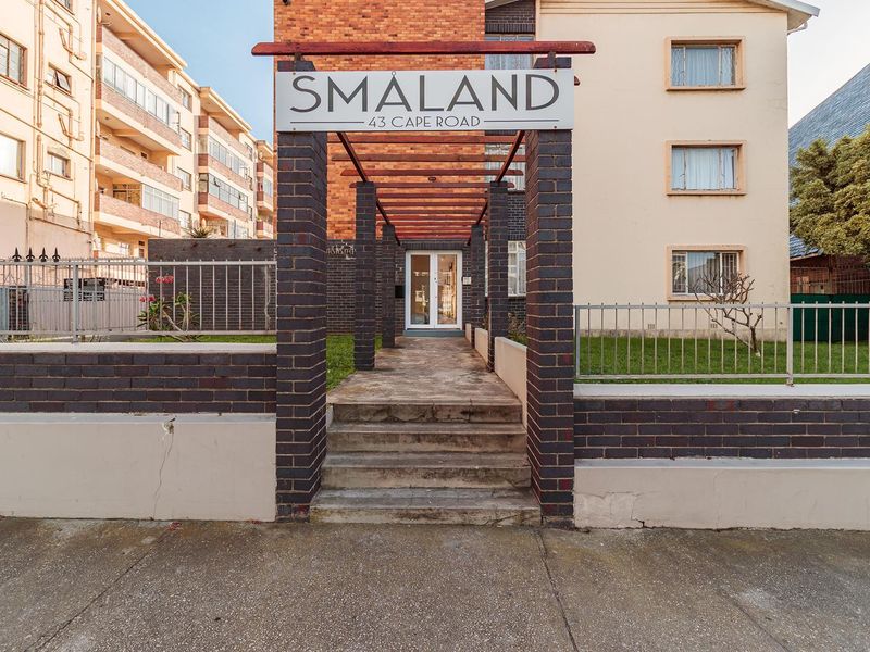 Front entrance view of Smaland apartment complex featuring a brick pillar walkway, timber pergola, and concrete stairs leading to the main building access.