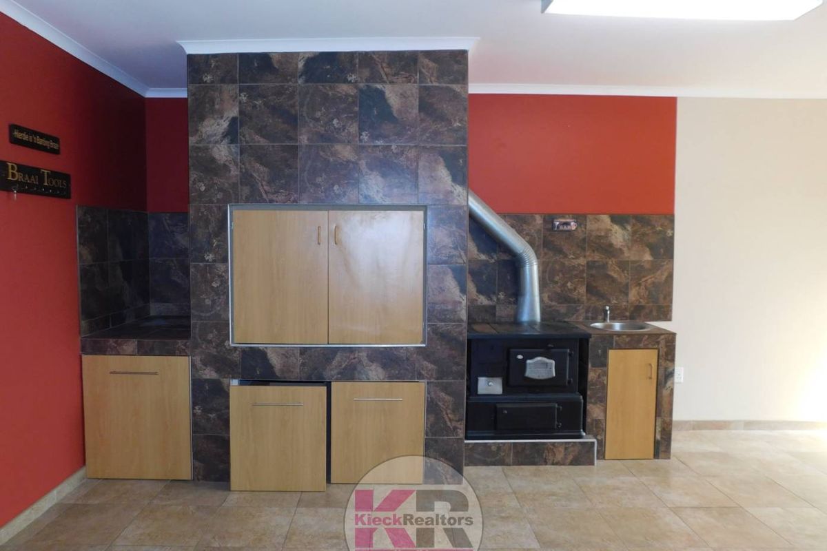 An indoor entertainment area featuring a built-in braai, wood-burning stove, tiled flooring, and integrated cabinetry with a small sink.