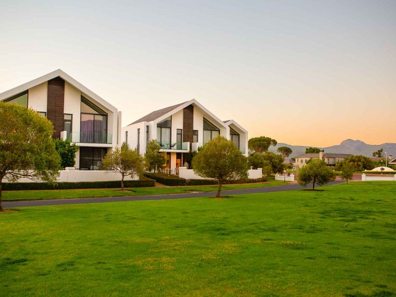 A scenic view of modern residential apartment buildings with pitched roofs, glass balconies, and manicured lawns in a well-maintained estate setting.