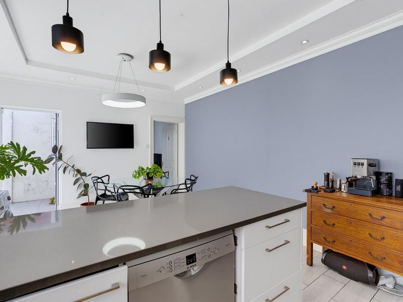 Modern open-plan kitchen area featuring a central island with stone countertop, integrated dishwasher, and stylish pendant lighting, flowing into the adjacent living space.