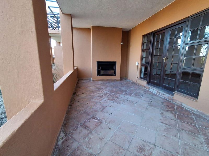 A covered patio area featuring a built-in braai, tiled flooring, and direct access to the interior through classic french doors.
