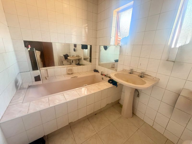 A dated bathroom featuring a built-in bathtub, pedestal washbasin, and full-height wall tiling, offering significant potential for a modern renovation.