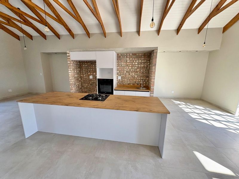 Spacious open-plan kitchen featuring a central island with a gas hob, exposed brick accents, and high vaulted ceilings with exposed timber beams.