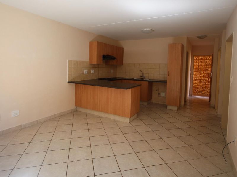 An open-plan kitchen and living area featuring tiled flooring, laminate cabinetry, and a breakfast counter, presenting a clean and functional blank canvas.