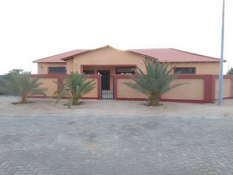 Front elevation of a single-story house featuring a tiled roof, perimeter boundary wall with a gated entrance, and a paved driveway.