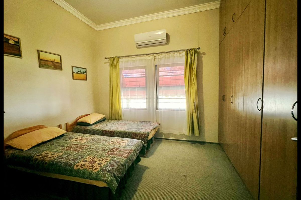 A bedroom featuring built-in wooden wardrobes, wall-mounted air conditioning unit, and carpeted flooring.
