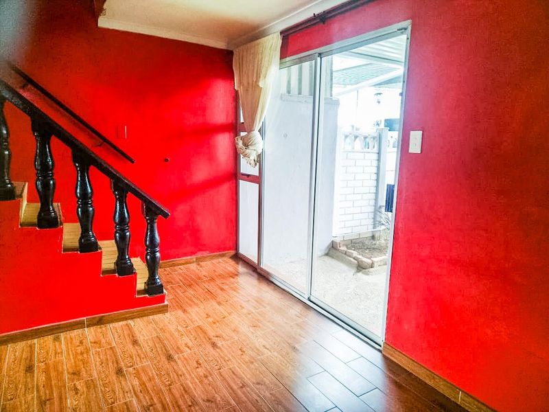 An empty entrance area featuring a wooden staircase with a dark balustrade, tiled flooring, and a sliding glass door leading to the exterior.