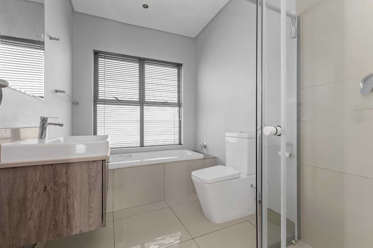 Modern bathroom featuring a vanity with basin, a built-in bathtub, a separate glass-enclosed shower, and a toilet, finished with neutral floor and wall tiles.