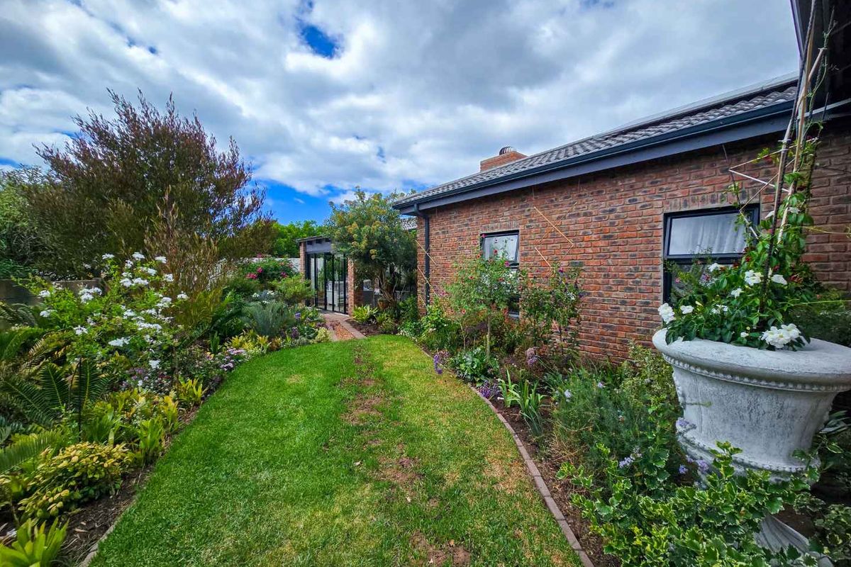 A well-maintained rear garden featuring a lush lawn, established flower beds, and a classic brick exterior facade with modern window frames.