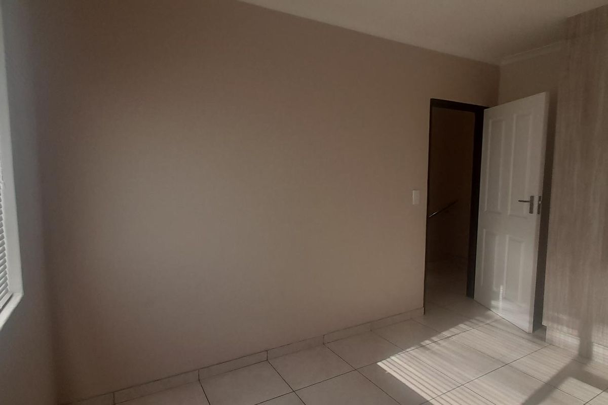 A bright bedroom featuring neutral tiled flooring, built-in wooden cabinetry, and venetian blinds on the window.