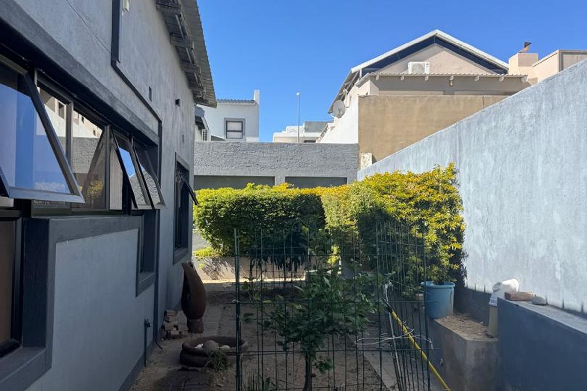A side exterior view of the property featuring a paved walkway, garden bed, and boundary wall.