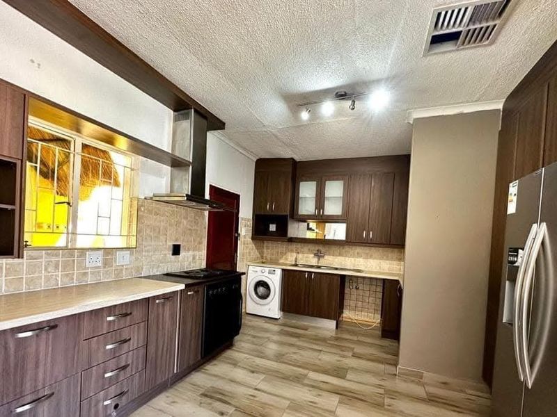 A functional kitchen featuring dark wood cabinetry, laminate countertops, tiled backsplash, and integrated appliances, offering a practical layout for daily meal preparation.