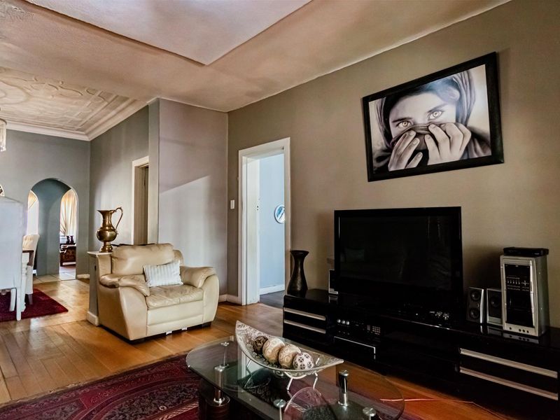 Spacious living room featuring hardwood flooring, decorative ceiling molding, and an elegant chandelier, with an open archway leading to the dining area.